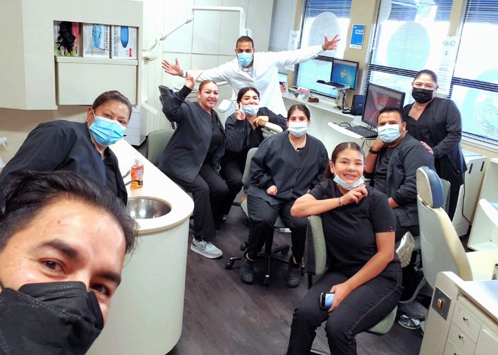 Meet the team: A group of dental clinic staff wearing masks and black uniforms pose together for a photo in a dental office.