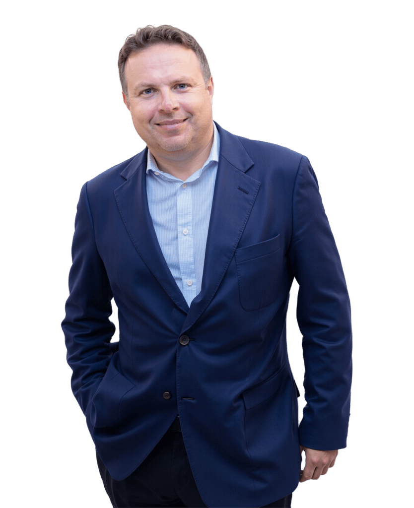 A man wearing a blue suit jacket and light blue shirt stands against a plain white background, smiling with one hand in his pocket—ready to explore new careers. Apply today and grow with us.